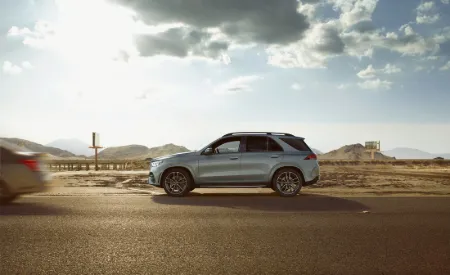 A blue Mercedes-Benz SUV drives through a field of wheat on a cloudless day.