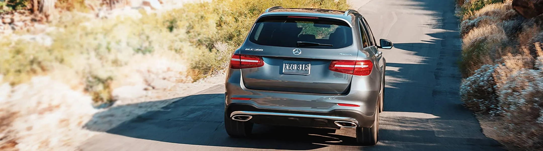 A gray Mercedes-Benz GLE SUV pulls away down a dusty road.